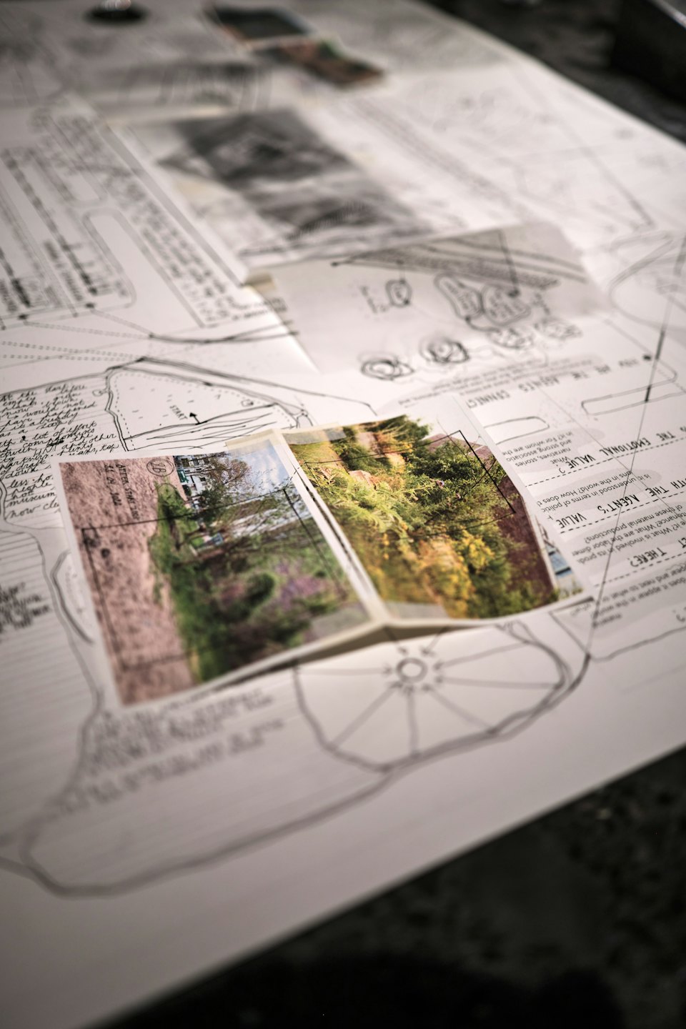 Architektonické plány a fotografie rozložené na tmavém stole.